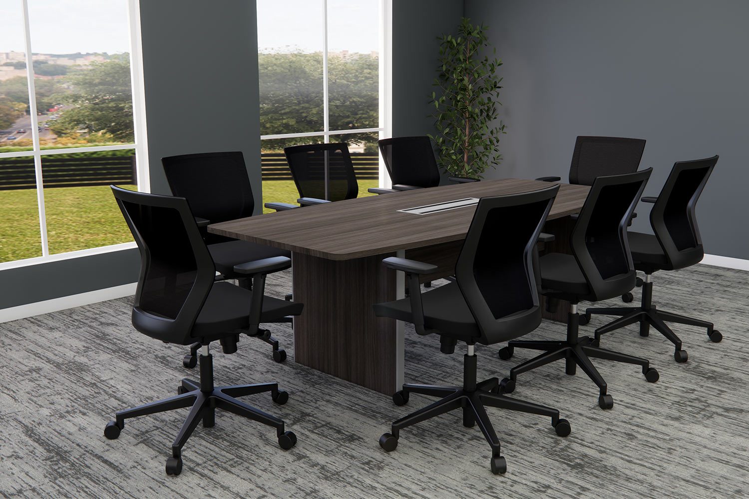 A modern conference room with a rectangular wooden table and eight black office chairs. Large windows provide a view of greenery outside. The room is decorated in muted tones with a plant in the corner and gray walls and carpet.